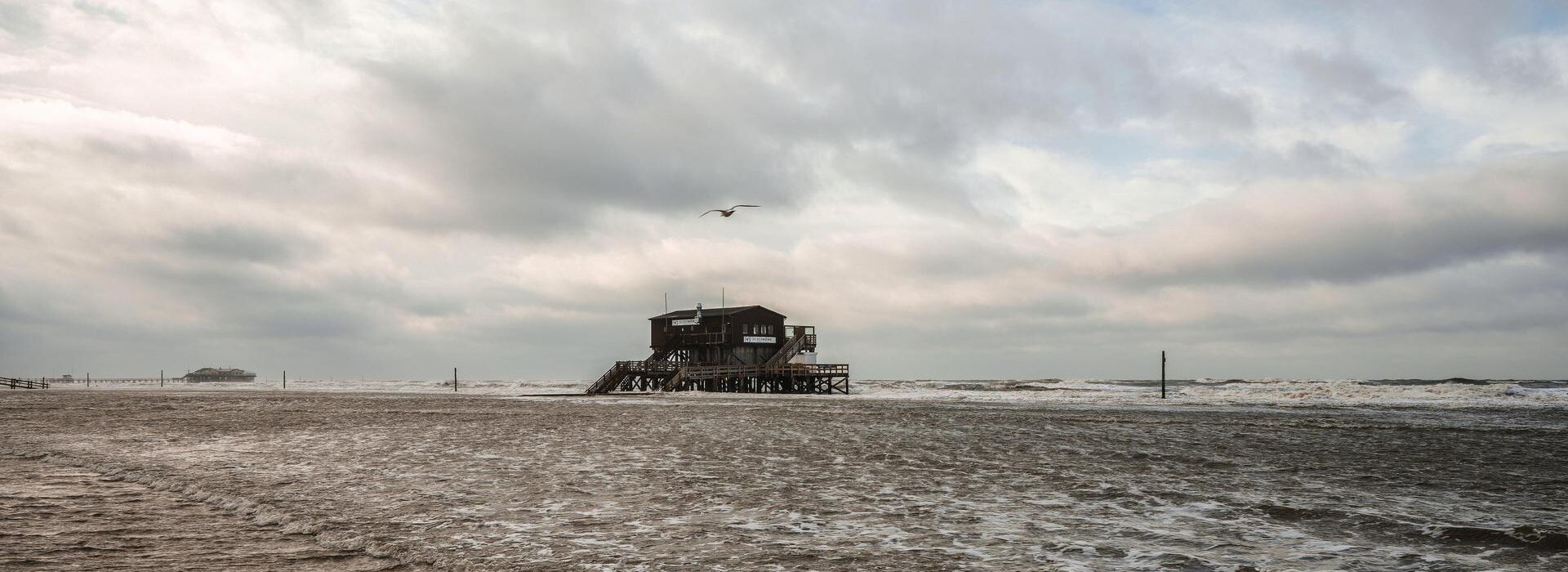 überspülter Strand mit Pfahlbau und grauem Himmel