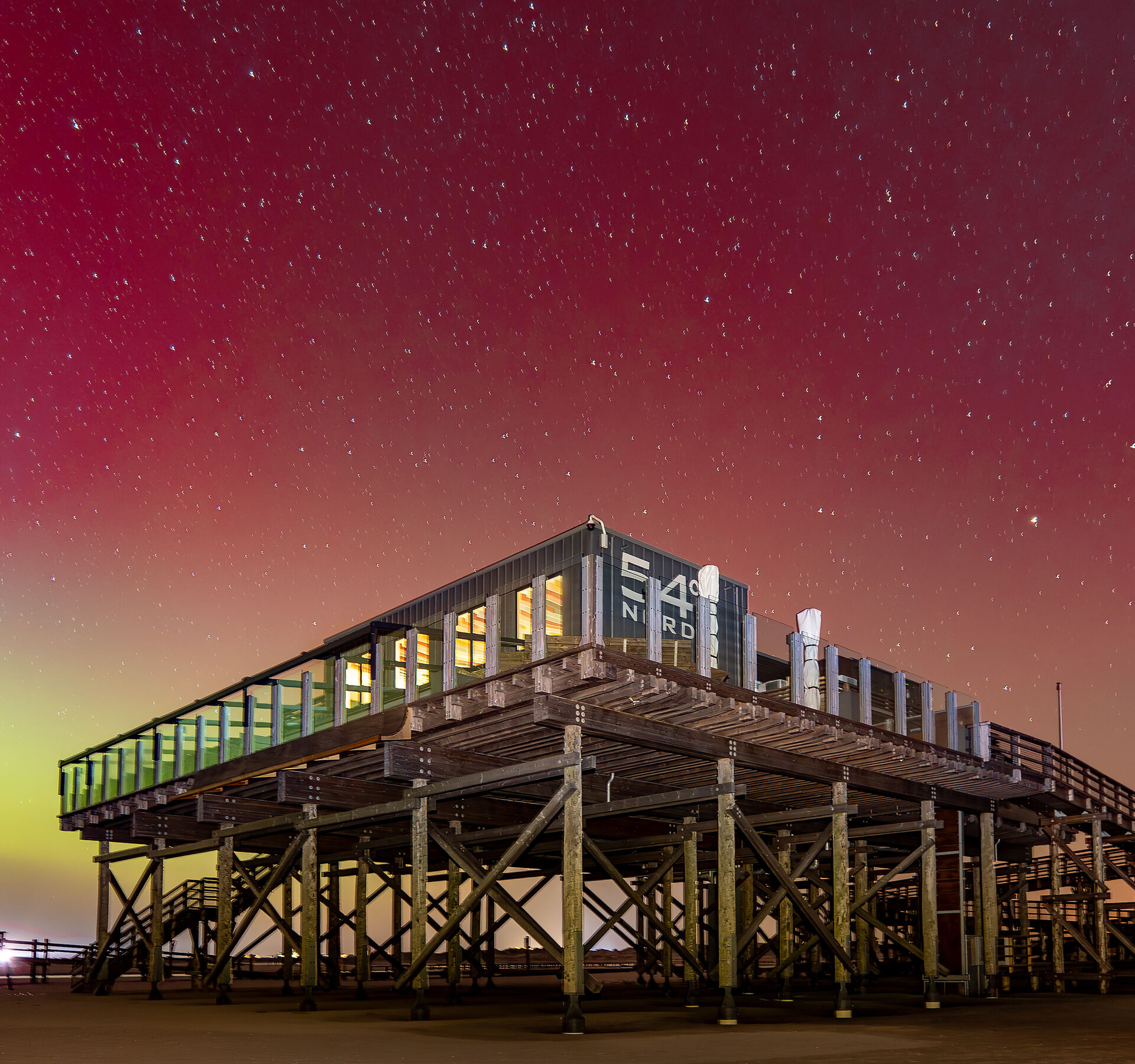 Polarlichter am Strand mit Pfahlbau im Vordergrund