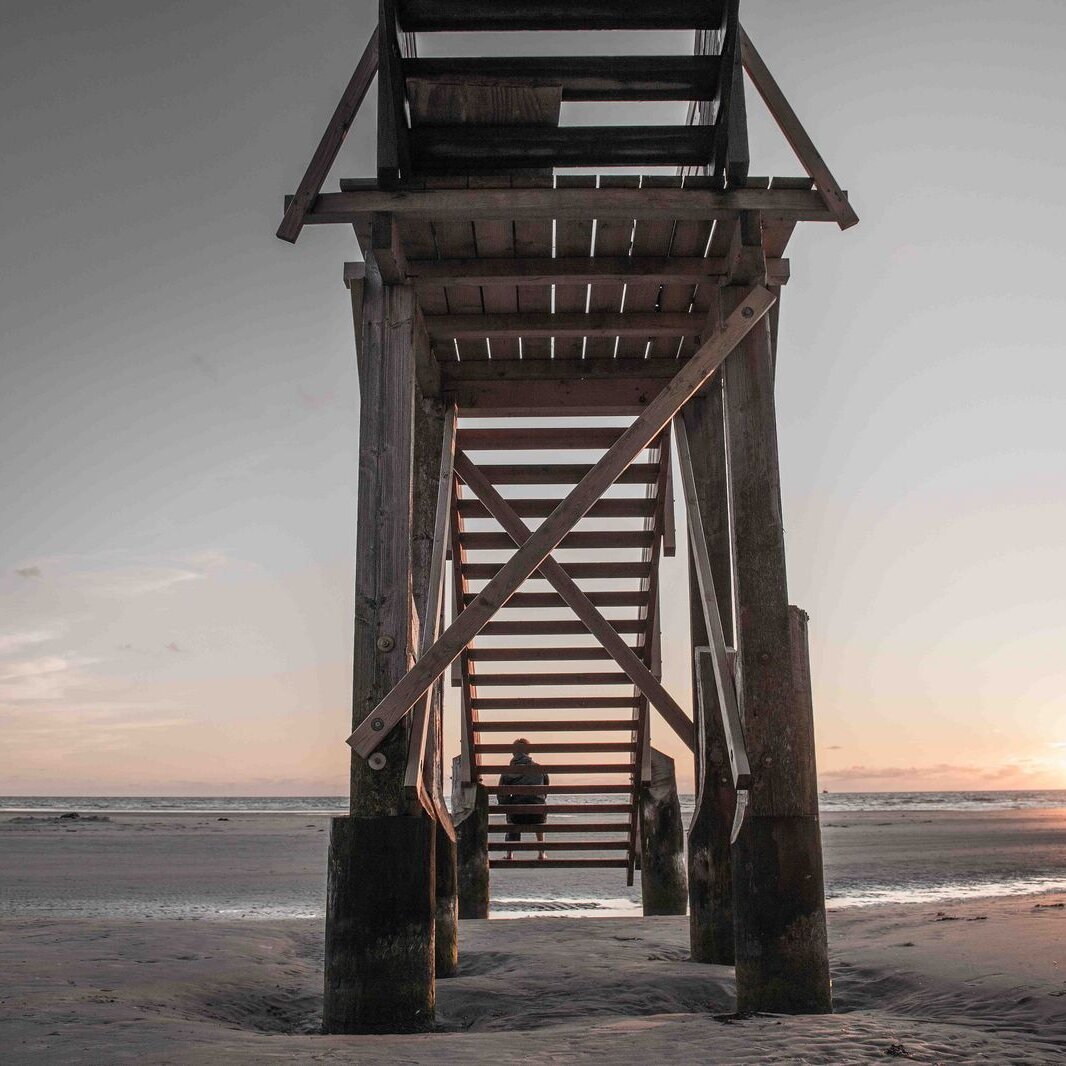 Mann sitzt auf der Treppe eines Pfahlbaus im Sonnenuntergang