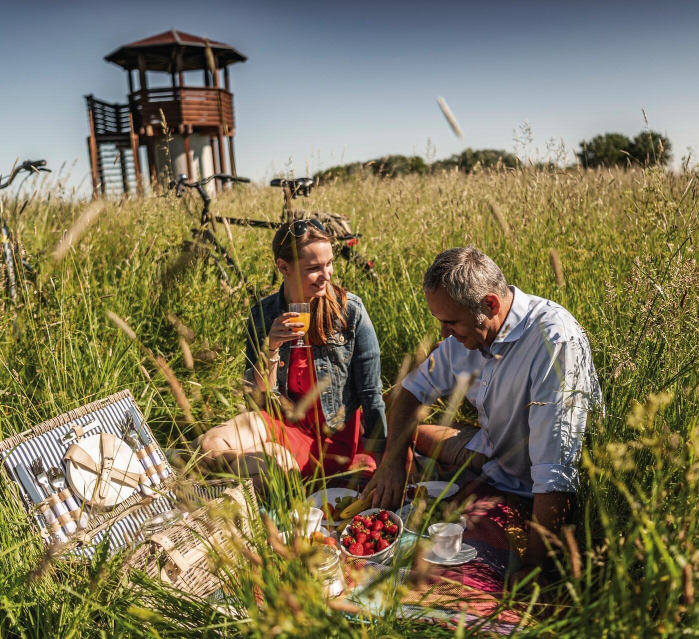 Paar beim Picknick auf einer Wiese vor einem Aussichtsturm