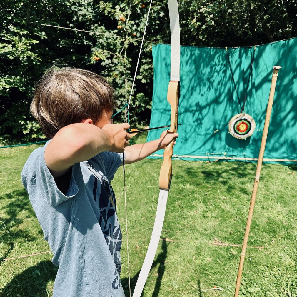 Ein Junge zielt mit Pfeil und Bogen auf eine Zielscheibe