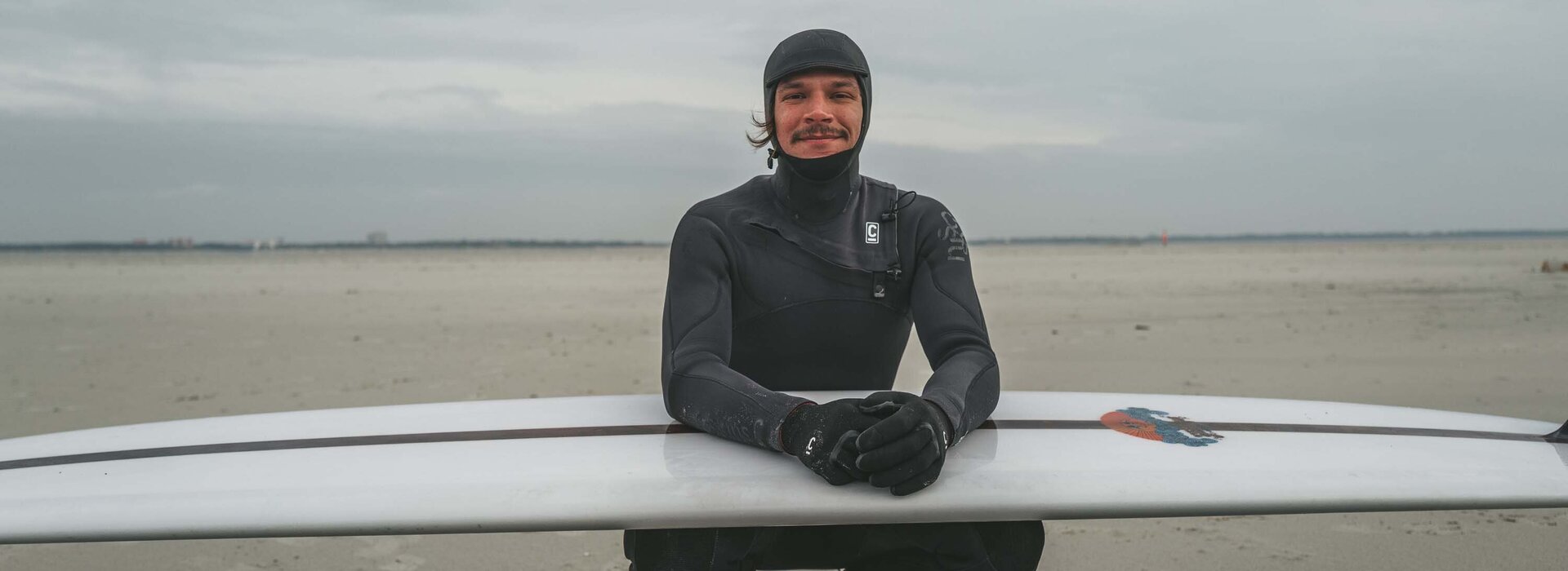 junger, sympathischer Surfer mit Surfbrett am herbstlichen Strand