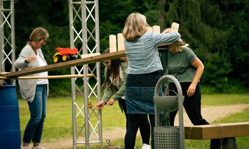 Personen bauen verschiedene Elemente auf eine Wippe.