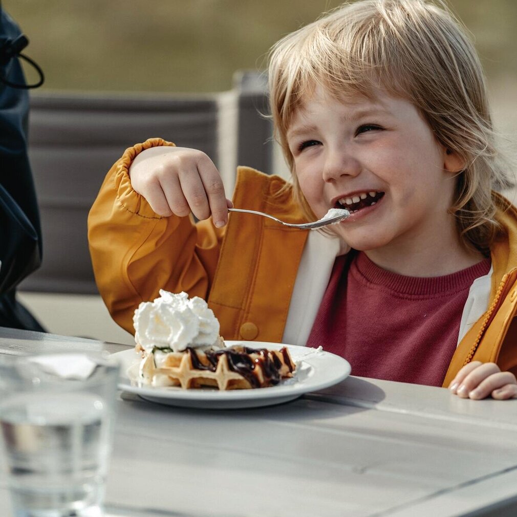 fröhliches Mädchen isst Waffel mit Sahne