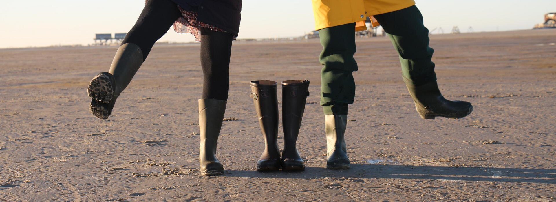 Personen mit Regenjacken und Gummistiefeln am Strand