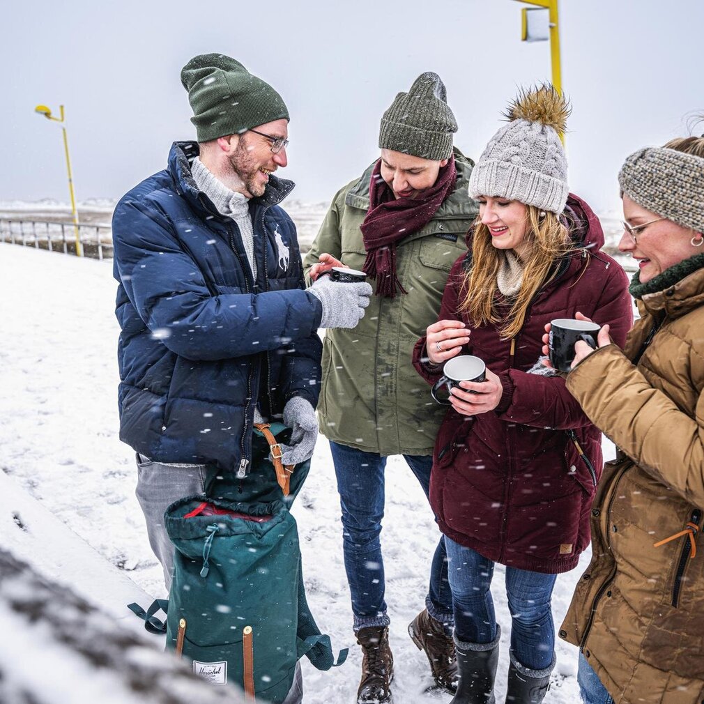 Freunde mit Heißgetränken an der Seebrücke bei Schnee