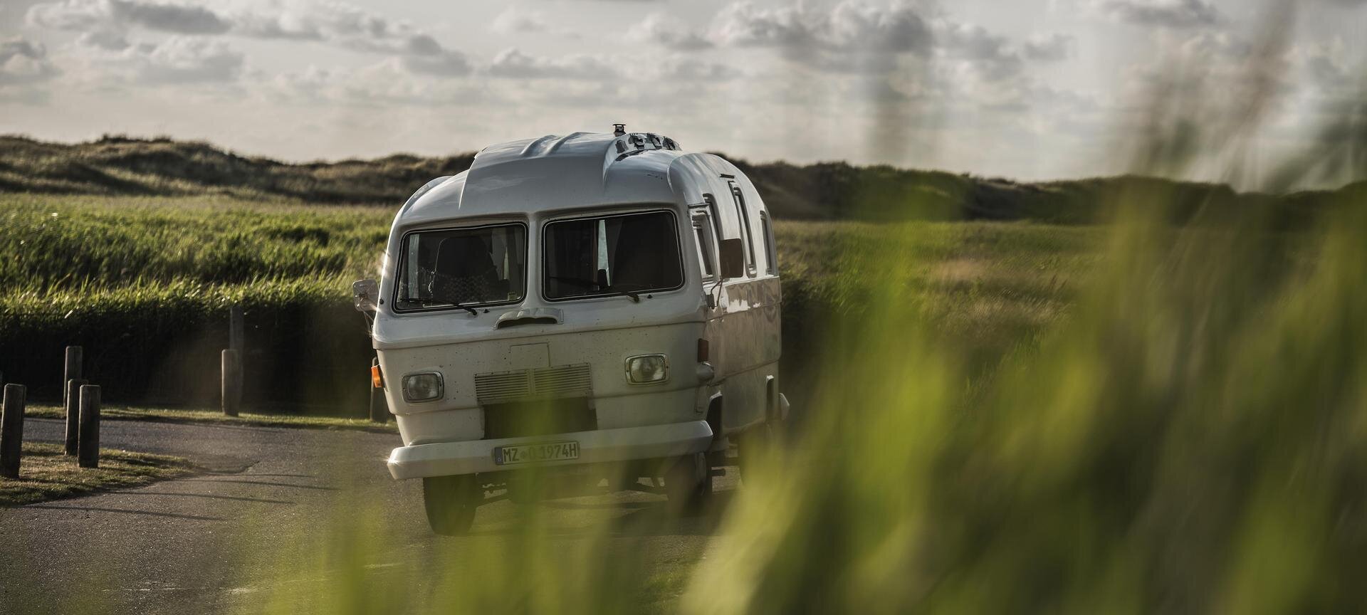 Oldtimer Bulli während der Fahrt mit Deich im Hintergrund