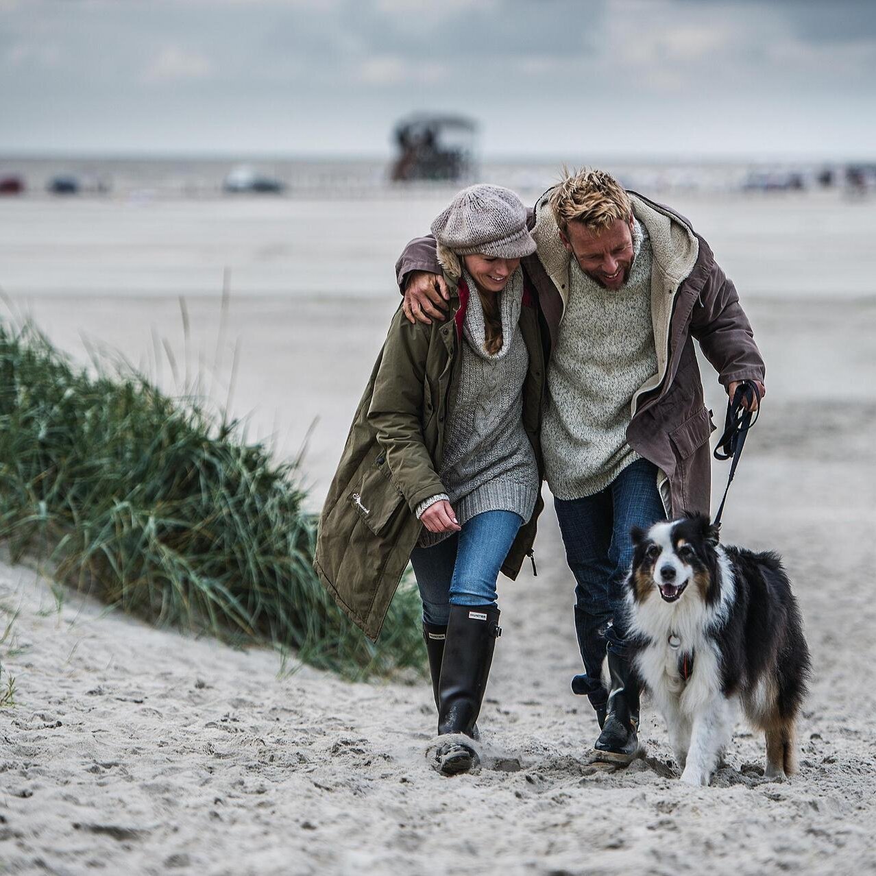 Paar läuft über den Strand mit Hund an der Leine