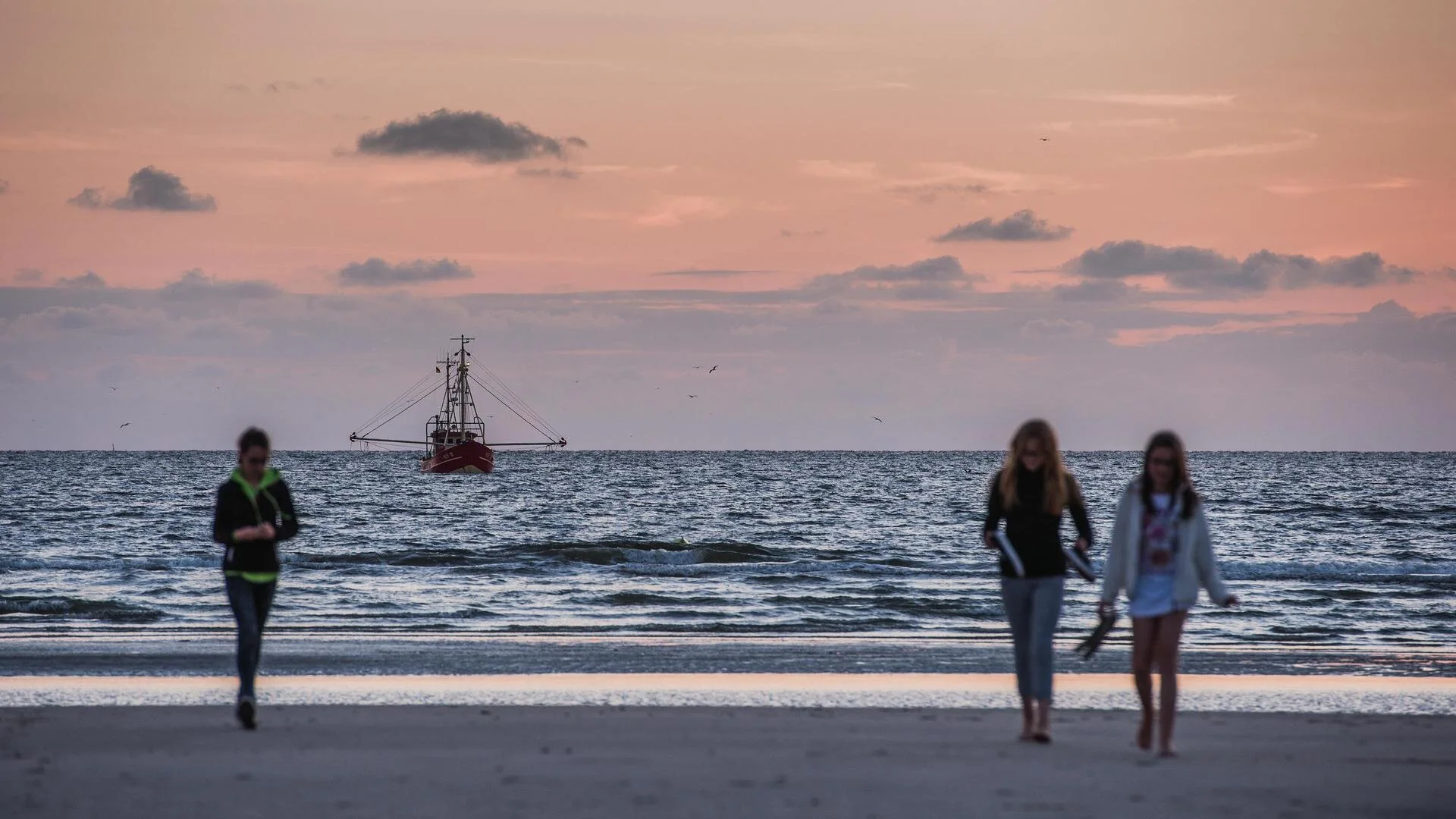 Menschen am Strand mit Kutter auf der Nordsee im Hintergrund