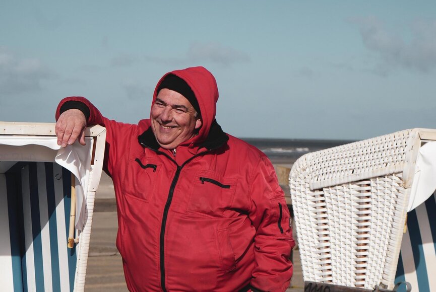 unser Strandmitarbeiter lehnt sich lachend an einen Strandkorb