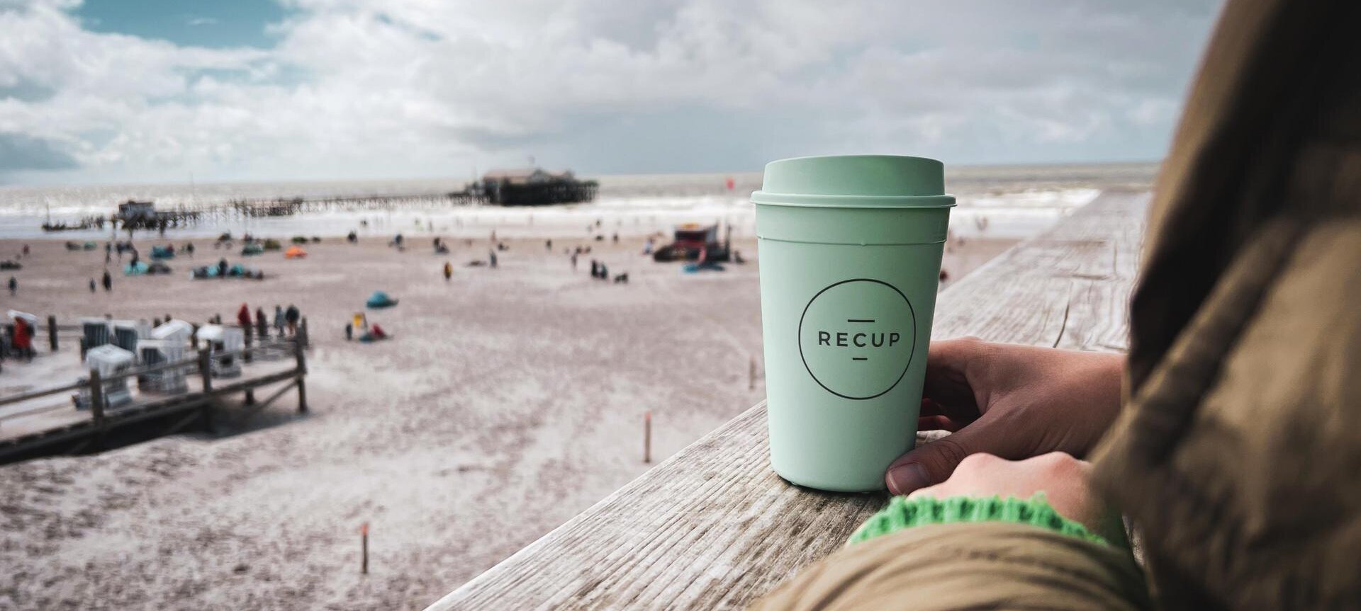 Dame mit einem RECUP Becher auf dem Mehrzweckgebäude am Ordinger Strand