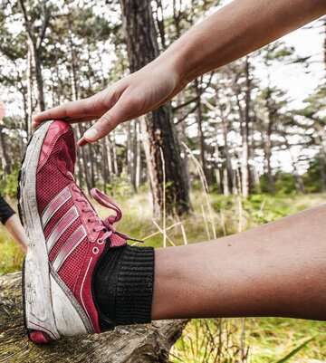 Frau beim Dehnen vorm Joggen im Wald