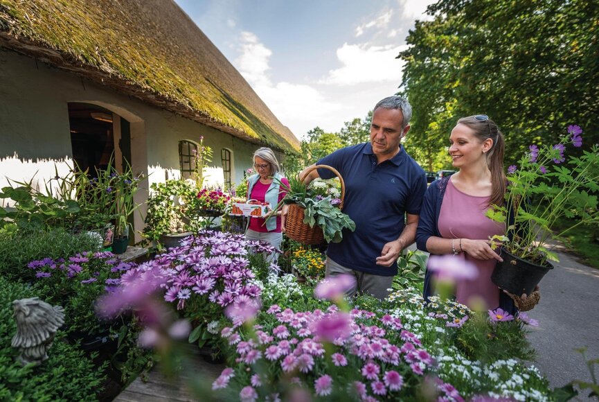 Paar kauft bunte Frühlingsblumen an einem Reetdachhaus
