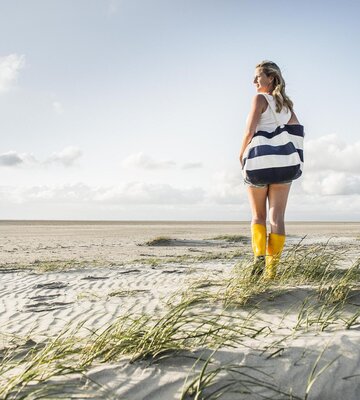Frau spaziert entlang der Dünen in gelben Gummistiefeln