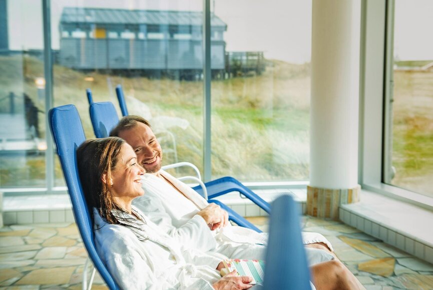 Paar entspannt auf Liegen im Ruhebereich mit Blick nach draußen