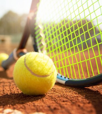Tennisschläger und Tennisball liegen auf dem Platz