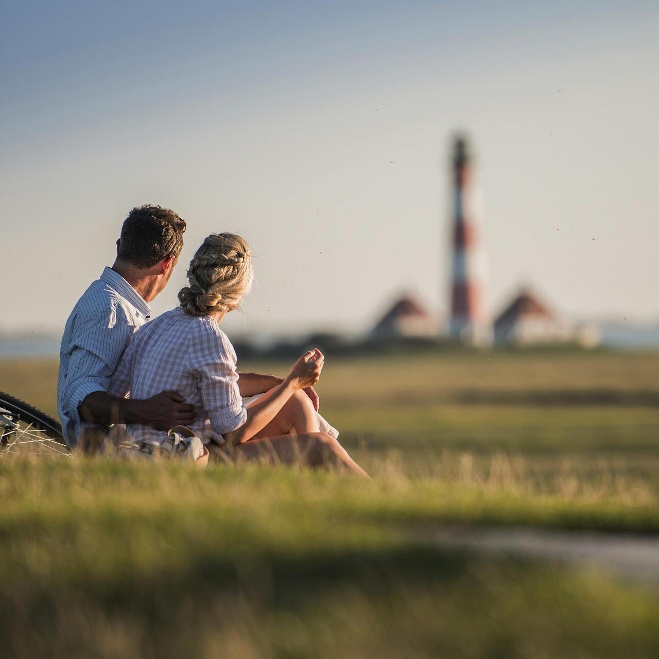 Paar sitzt auf dem Deich und blickt auf den Leuchtturm Westerhever