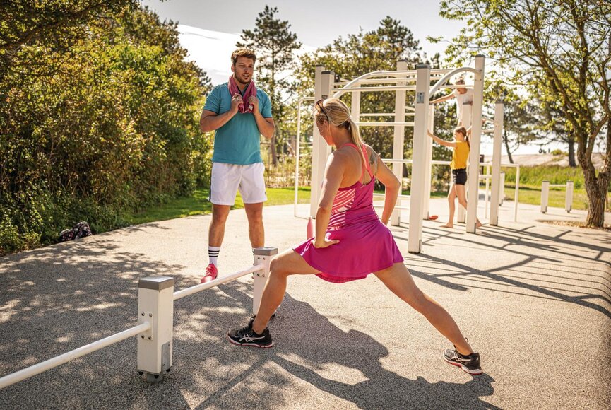 Frau und Mann beim Dehnen vor Outdoor-Sportgeräten