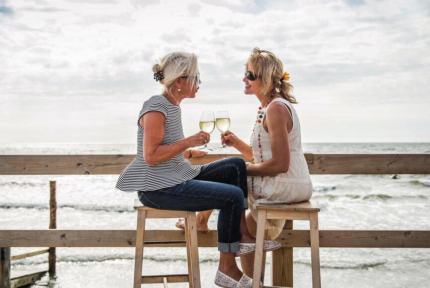 Freundinnen auf einem Pfahlbau mit zwei Gläsern Wein beim Quatschen