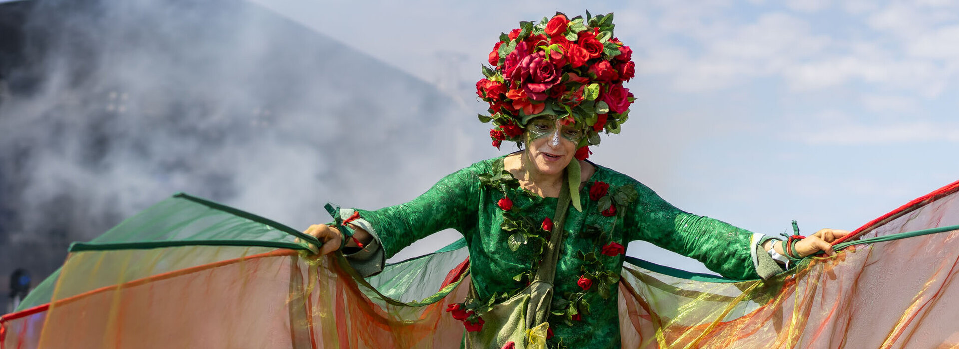Ein Blumenfee auf Stelzen schwingt ihre Tücher und begrüßt ein kleines Kind