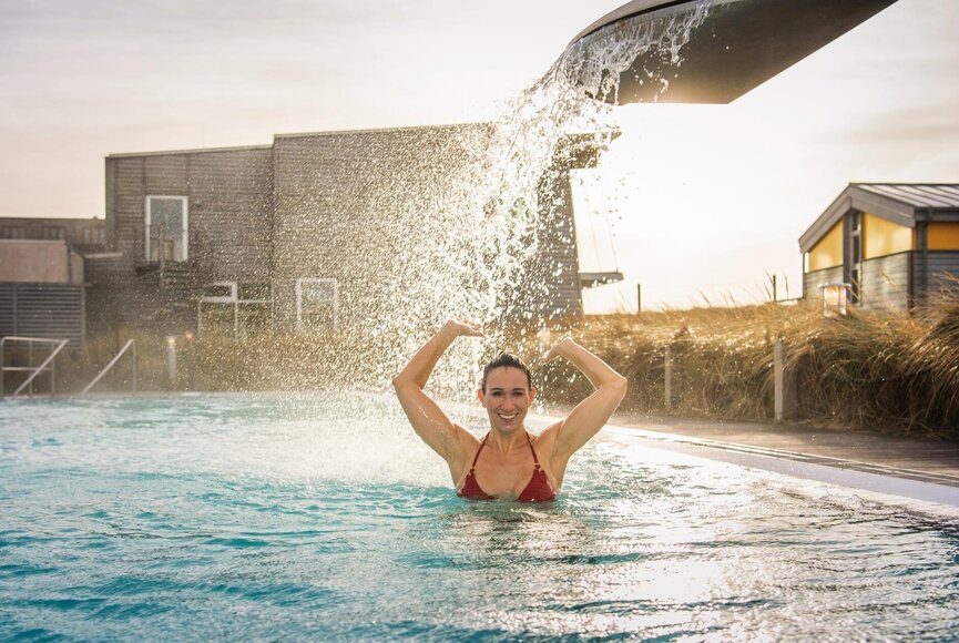 Frau unter der Schwalldusche im Außenbecken