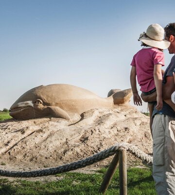Familie schaut sich eine große Sandskulptur in Form eines Wals an