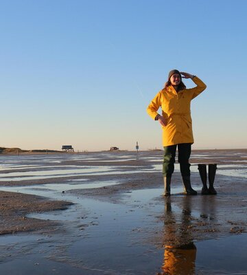 junger Mann mit gelbem Friesennerz und Gummistiefeln am Strand