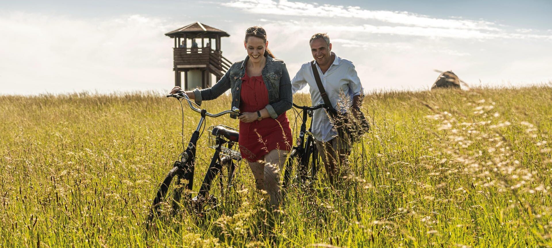 Pärchen mit Fahrrädern auf einer Wiese mit Aussichtsturm