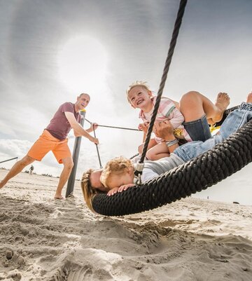 A family having fun at the beach playground on a nest swing