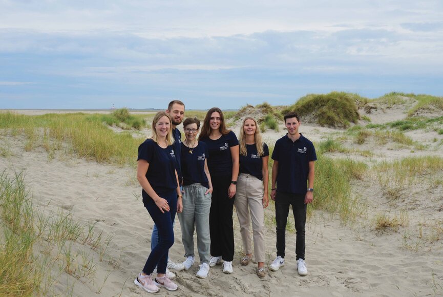 Gruppenfoto von Tourist-Info-Mitarbeitern am Strand in den Dünen. 