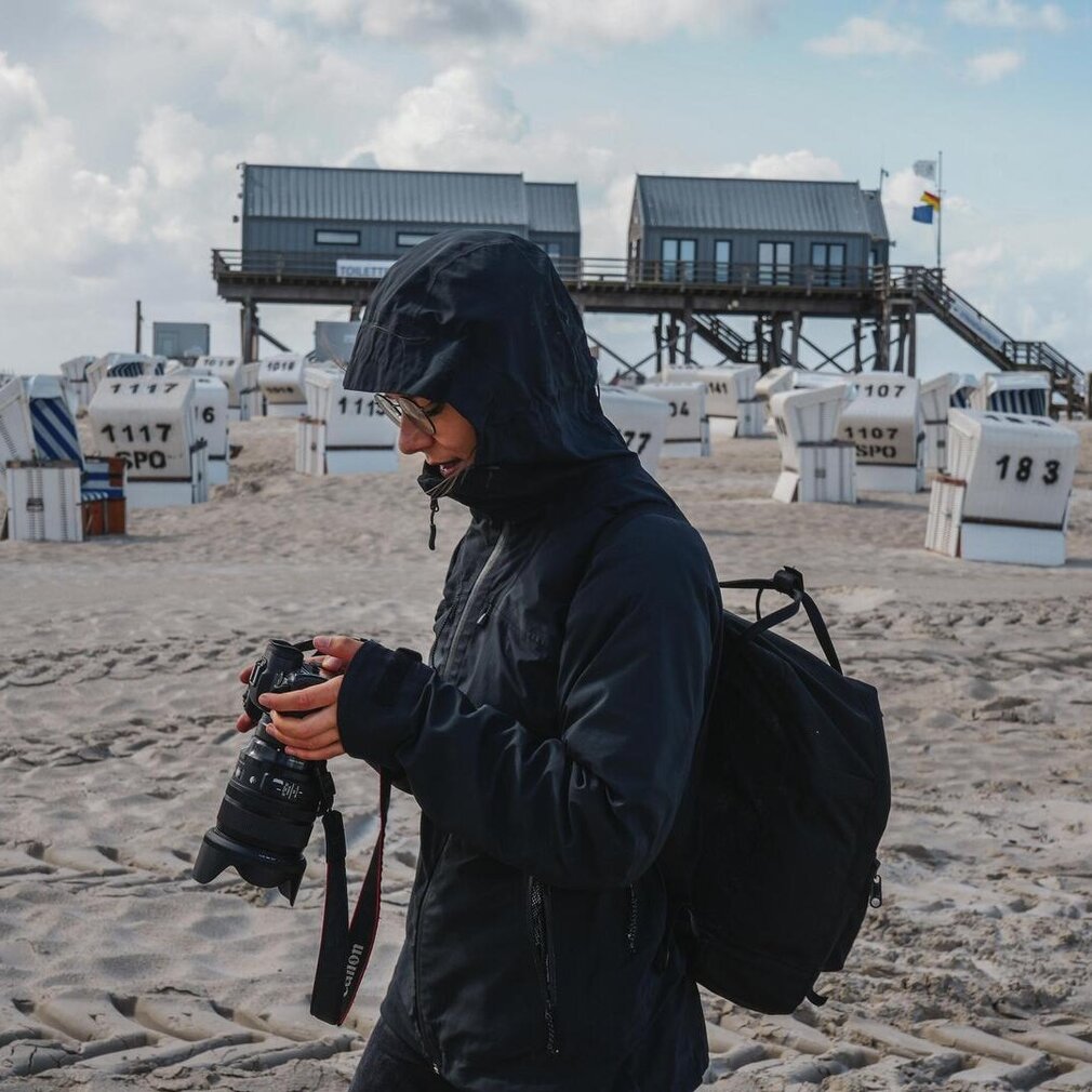 Marina steht in Regenkleidung vor dem Pfahlbau am Ordinger Strand