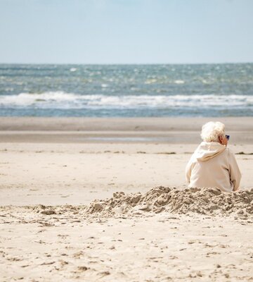 Frau sitzt am Strand und blickt in die Wellen